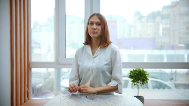 Massage - mooie en jonge masseuse vrouw zit met haar handen op de bank — Stockvideo