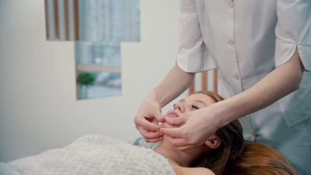 Massage - Massagemeister knetet Nasolabialfalten auf dem Gesicht einer jungen Frau — Stockvideo