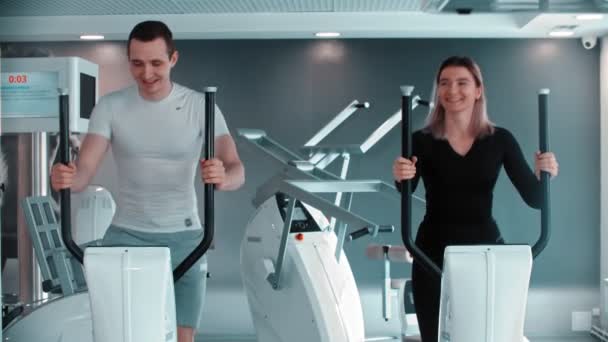 Современный тренажерный зал - мужчина и женщина делают утренние упражнения в тренажерном зале и разговаривают — стоковое видео