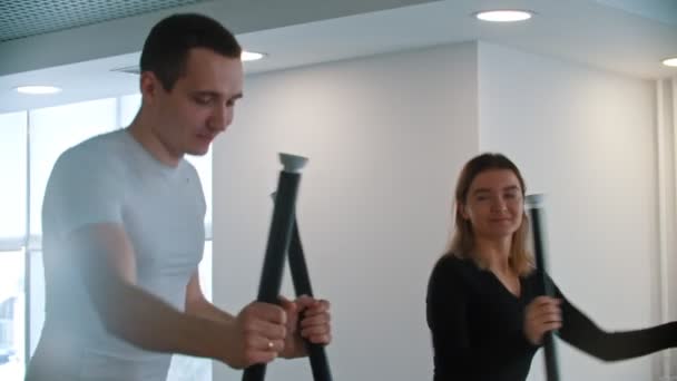 Gimnasio moderno: un tipo con camiseta blanca y una mujer haciendo ejercicios matutinos en el gimnasio y riéndose — Vídeos de Stock
