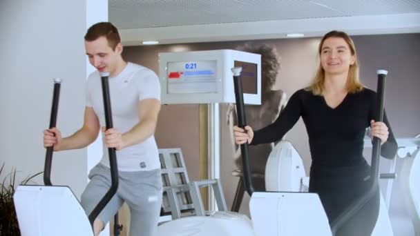 Moderne fitnessruimte - sporter en sportvrouw die ochtendoefeningen doet in de fitnessruimte en lacht — Stockvideo