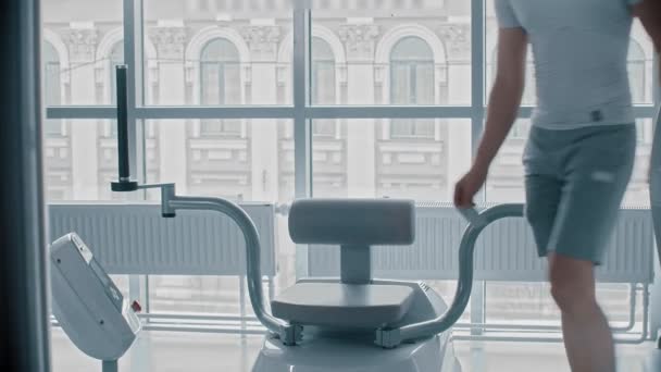 Moderne fitnessruimte - jonge man zitten op het trainingstoestel en wachten op wanneer het mogelijk zal zijn om te beginnen — Stockvideo