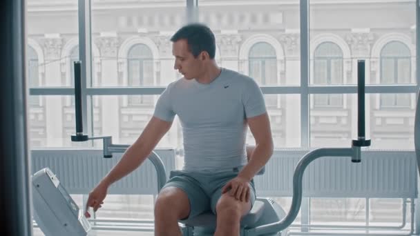 Σύγχρονο γυμναστήριο - ένας τύπος κάθεται στη συσκευή κατάρτισης και περιμένει πότε θα είναι δυνατόν να ξεκινήσει — Αρχείο Βίντεο