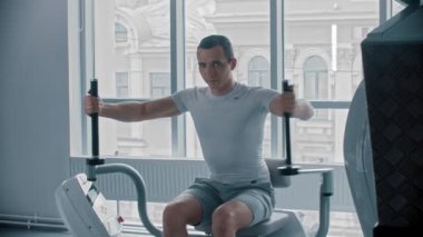 Modern spor salonu. Spor salonunda kol egzersizi yapan beyaz tişörtlü genç bir adam.