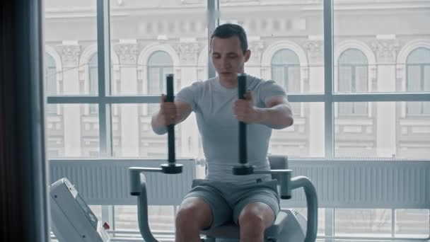 Σύγχρονο γυμναστήριο - ένας νεαρός άνδρας σε λευκό t-shirt κάνει άσκηση βραχίονα στη συσκευή κατάρτισης — Αρχείο Βίντεο
