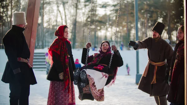 Русский фольклор - молодая женщина качается и все смеются в солнечный день — стоковое фото