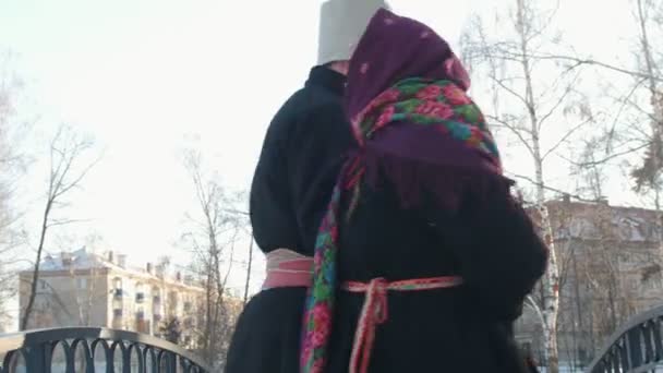 Folclore russo - homem e mulher em trajes tradicionais russos estão dançando na ponte no inverno — Vídeo de Stock