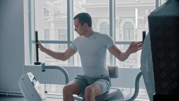 Moderne fitnessruimte - een man die op het trainingstoestel gaat zitten en zijn handen traint — Stockvideo