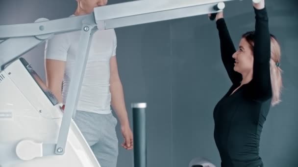Тренировка с инструктором по фитнесу в тренажерном зале - молодая женщина тренирует руки - тренер корректирует ее позу — стоковое видео