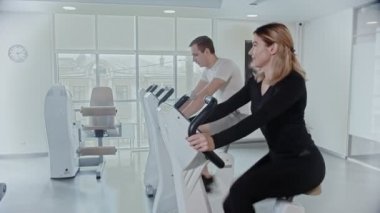 Sportif erkek ve kadın, modern beyaz spor salonunda bacaklarını egzersiz bisikleti ile çalıştırıyor.