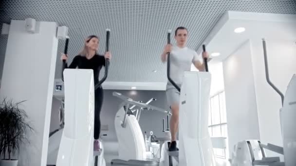 Hombre y mujer deportistas entrenando sus piernas en bicicleta estática en un moderno gimnasio blanco — Vídeos de Stock