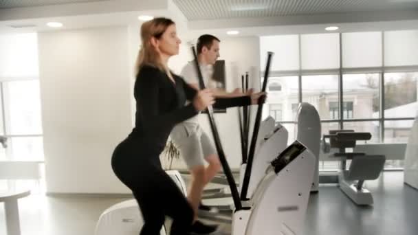 Спортивные юноши и девушки в спортивной одежде тренируют ноги на велотренажере в современном тренажерном зале — стоковое видео