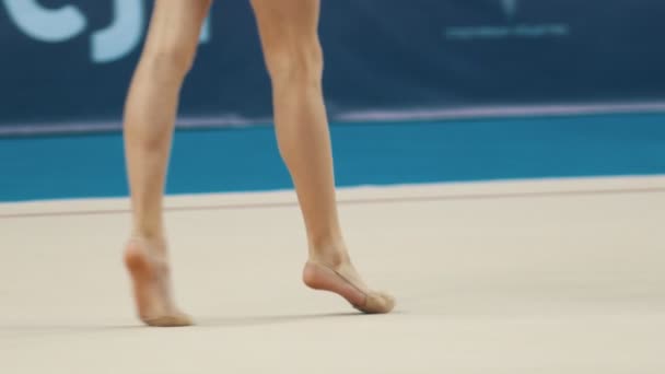Las piernas de las mujeres jóvenes en los torneos de gimnasia rítmica chica en traje de baño deportivo caminando en el escenario y rueda la pelota a otra chica — Vídeos de Stock