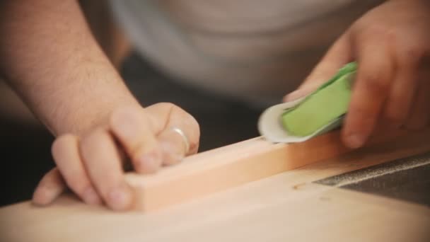 Trabajo de carpintería - manos del trabajador del hombre puliendo la plancha de madera con un papel de lija — Vídeo de stock