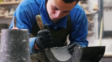 Beton atölyesi. Adam siyah beton döküm kalıbını spatulayla temizliyor.