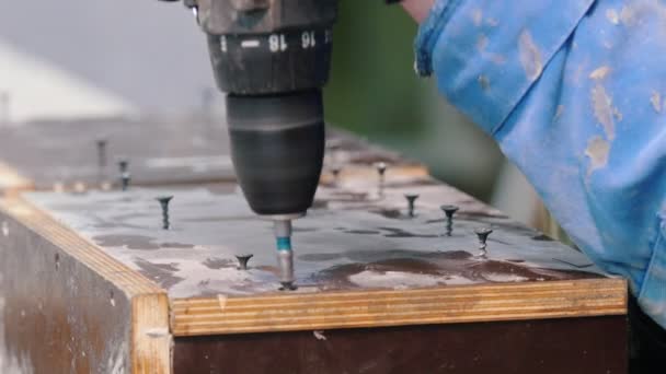 Бетонная мастерская - человек с отвёрткой, вкручивающий болты в деревянную поверхность — стоковое видео