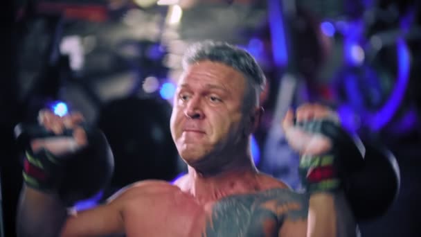 Een volwassen man bodybuilder uitvoeren tillen zware kettlebells putting inspanning — Stockvideo