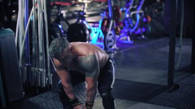Gri saçlı sert bir adam spor salonunda kettlebell çekiyor.