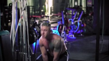 Dövmeli sert bir vücut geliştirme ustası spor salonunda kettlebell çekiyor.