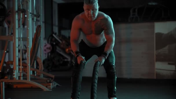 Een volwassen stoere man bodybuilder vechten touwen in de sportschool — Stockvideo