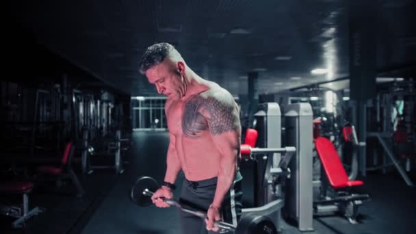 Un homme dur avec bodybuilder cheveux gris tire un haltère dans la salle de gym sombre — Video