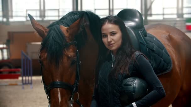 Hippodrome - jonge vrouw die naast haar paard staat en een helm in haar handen houdt — Stockvideo