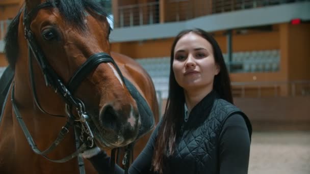 Hipodrom - młoda jeźdźca stojąca z koniem i patrząca w kamerę — Wideo stockowe