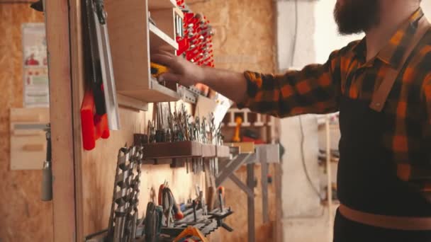 Bearded man worker takes roulette from the stand in the carpentry workshop — Stock Video