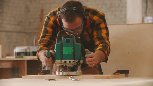 Carpentry industry - man worker in protective glasses and headphones grinding a wooden item — Stock Video