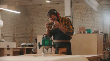 Marangozluk endüstrisi - işçi önlüğünü ve koruyucu gözlüklerini takar ve öğütme makinesiyle çalışmaya başlar