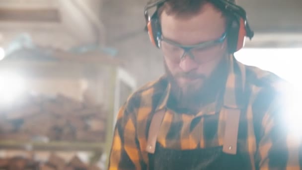 Lavoratore barbuto tagliare il legno con una sega circolare in officina spingendo la tavola di legno con un bastone di plastica — Video Stock