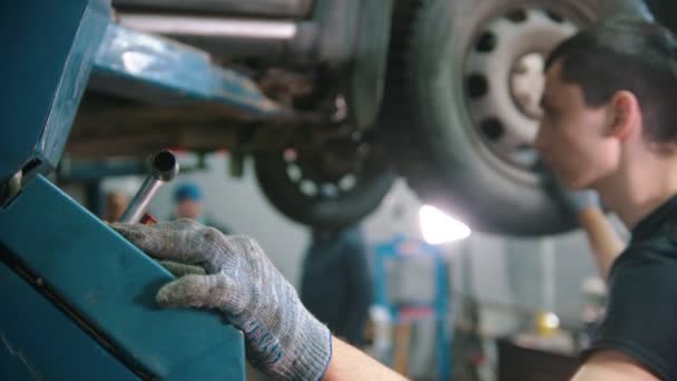 Auto reparation verkstad - ung man arbetare lyfta bilen upp — Stockvideo