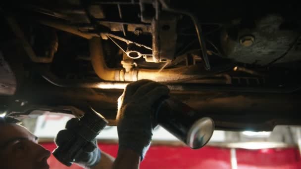 Auto reparatiewerkplaats - man die onder de auto werkt - sproeien van een anti-oxidatie desinfectiemiddel onder de auto en het verwijderen van het vuil — Stockvideo