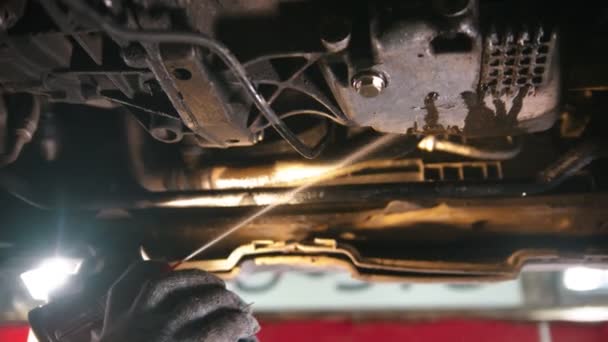 Taller de reparación de automóviles - el hombre que trabaja bajo el coche - pulverización de un desinfectante anti-oxidación debajo del coche y la eliminación de óxido y suciedad — Vídeo de stock