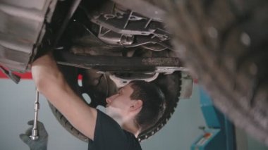 Otomobil tamircisi - İngiliz anahtarıyla arabanın altında çalışan genç adam.
