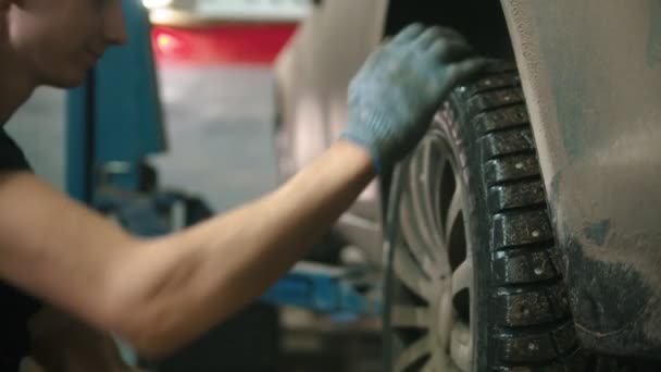 Taller de reparación de automóviles - joven con guantes desenrosca la rueda del coche — Vídeo de stock