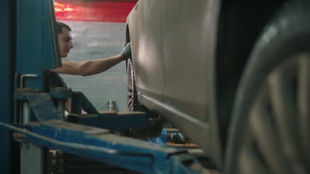Auto κατάστημα επισκευής - νεαρός άνδρας με γάντια αποσυνδέει τον τροχό από το αυτοκίνητο — Αρχείο Βίντεο
