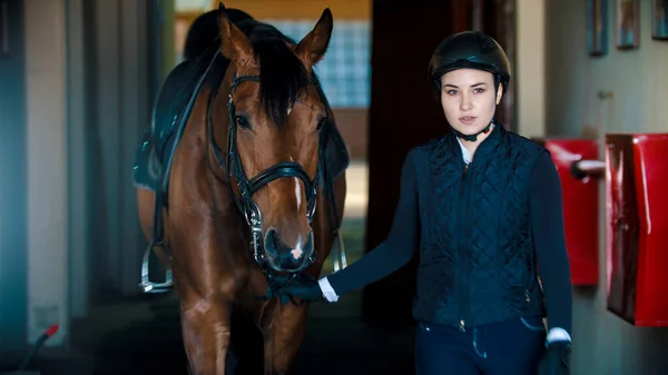 Ипподром - молодая всадница, стоящая с лошадью и смотрящая в камеру — стоковое фото