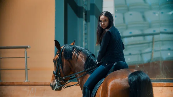 Uma mulher montando um cavalo marrom escuro no hipódromo — Fotografia de Stock