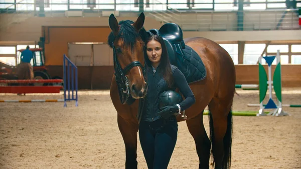 Ипподром - молодая улыбающаяся женщина-всадник, стоящая с лошадью и смотрящая в камеру — стоковое фото