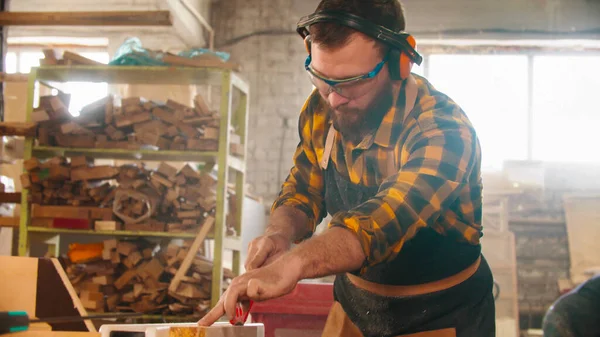 Homme barbu dans des lunettes de protection coupant un morceau de bois avec une scie circulaire — Photo