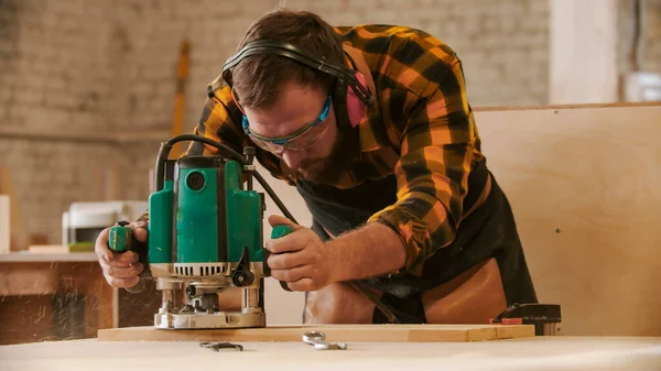 Столярная промышленность - человек в защитных очках и наушниках, вырезающий узоры из деревянной доски — стоковое фото