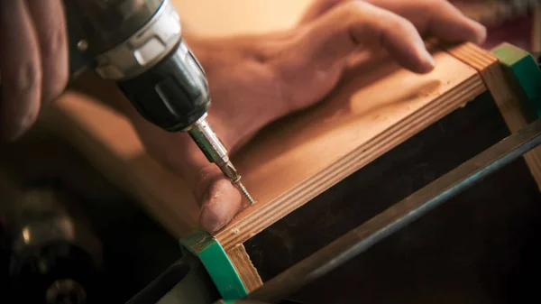 Carpentry working - man worker drills screws into the piece of plywood — Stock Photo, Image