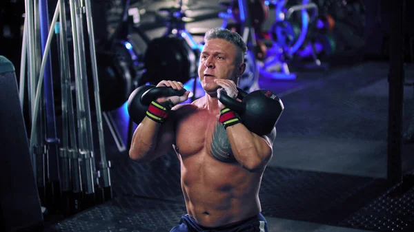 An adult shirtless man bodybuilder performing lifting heavy kettlebells — Stock Photo, Image