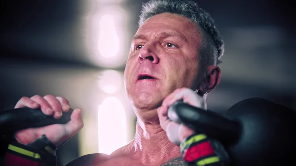 Difícil homem adulto com cabelo grisalho colocando esforço em levantar kettlebells — Fotografia de Stock