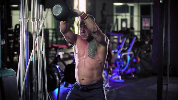 A tough man bodybuilder with a tattoo pulls a kettlebell in the gym
