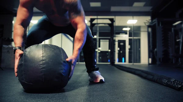 An adult man bodybuilder lifting a heavy ball in the gym — Stock Photo, Image