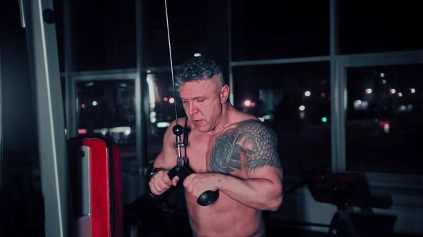 Жорсткий чоловік з татуюванням на плечі тренує руки в тренажерному залі за допомогою тренувального симулятора рук — стокове фото