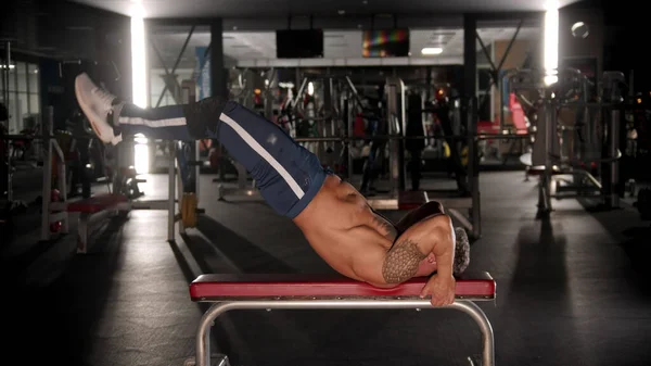 An adult man bodybuilder training his back and stamina in the gym lying on the bench — Stock Photo, Image