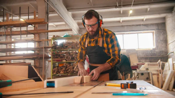 Bearded man skära trä med hjälp av en cirkelsåg i verkstaden — Stockfoto